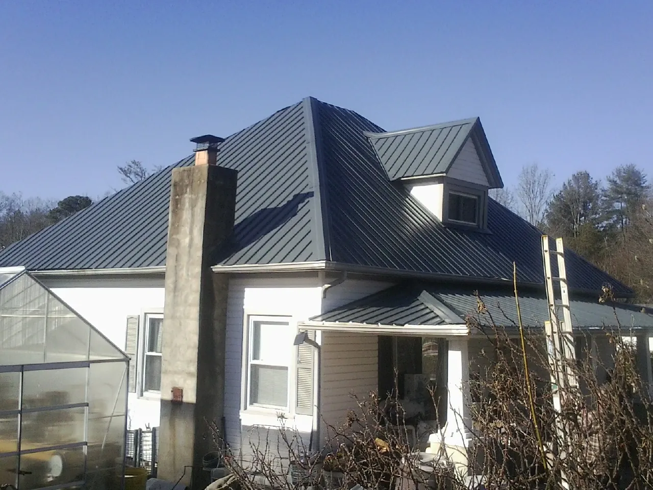 Dark blue standing seam metal roof on a white farmhouse with dormer — Slate & Tile Roof Repair by Roofing Brothers in Hill City