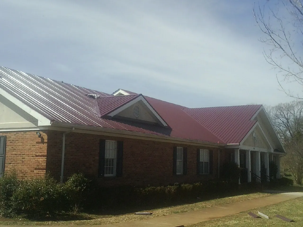 Red metal roof with gabled entries on a long brick building, from a Hail Damage Roof Repair job in Hill City