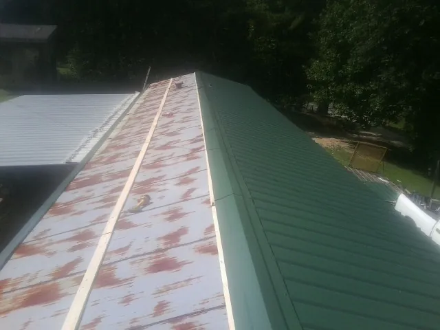 Old rusted panels beside newly installed green metal roofing — Wind Damage Roof Repair by Roofing Brothers in Hill City