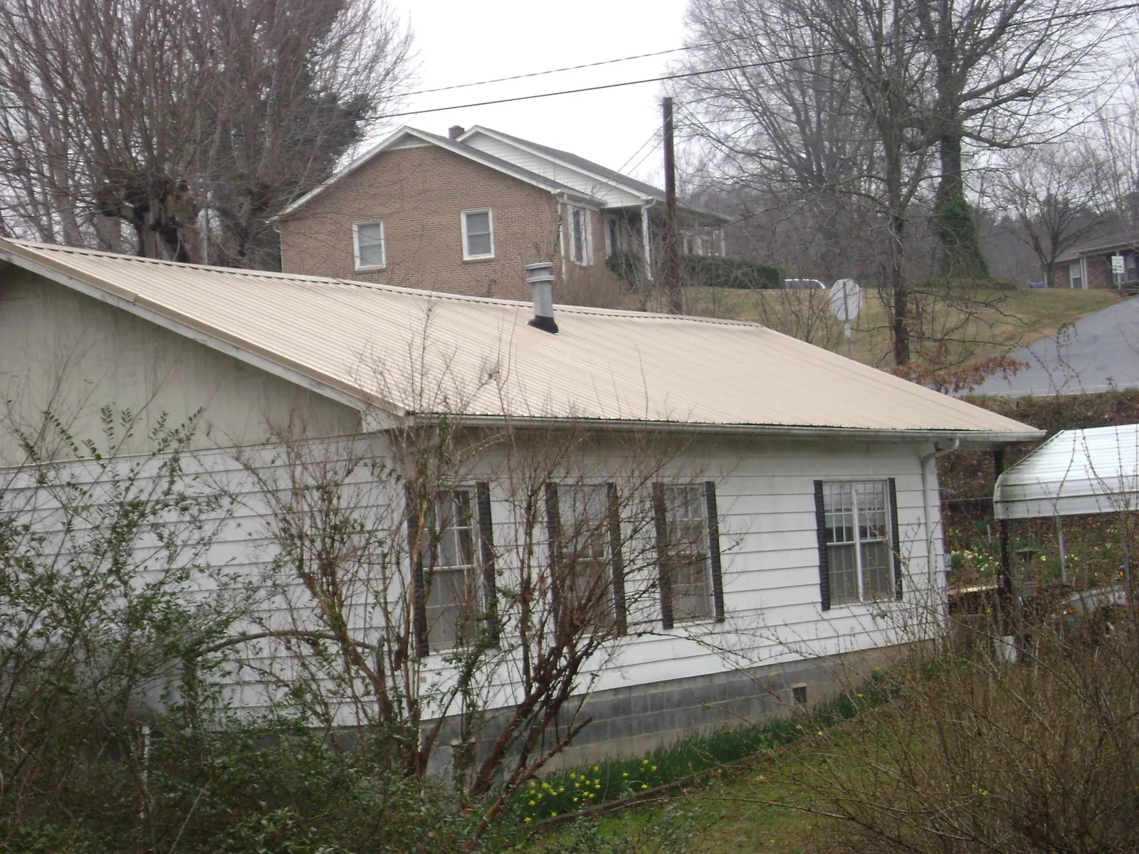 Tan metal roof on a white sided house set into a hillside — Commercial Roofing by Roofing Brothers in Hill City